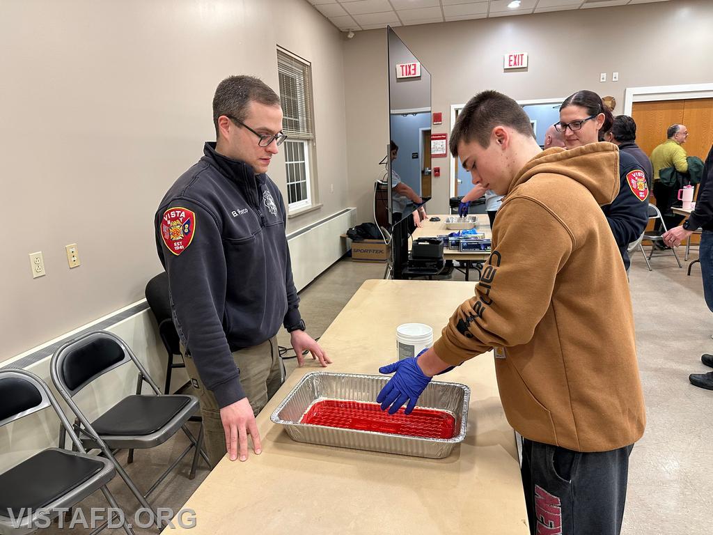Probationary Firefighter Teddy Goetz practices taking off his "blood soaked" medical gloves as Assistant Chief Brian Porco looks on
