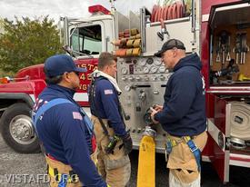 Captain Marc Baiocco reviewing the Engine 142 pump panel with Probationary Firefighter Paul Rossi, alongside Foreman Martin Rojas