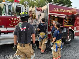 Foreman Brian Sferra reviewing the Engine 142 pump panel with Firefighter/EMT Ashtin Rama and Probationary Firefighter/EMT Candidate Hanna Zhao as Firefighter Phil Wanderman looks on